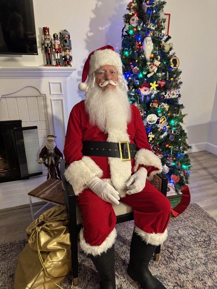 Santa Claus seated by the fireplace and Christmas tree with his gold gift sack