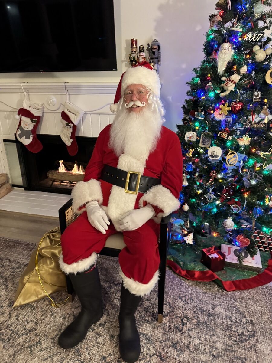Santa Claus seated beside a fireplace with hanging stockings