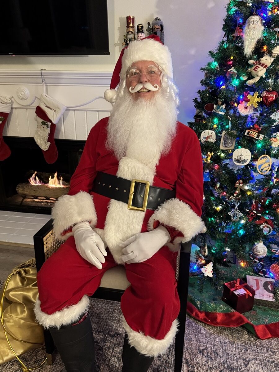 Santa Claus with gloved hands resting on his knees in front of a glowing tree