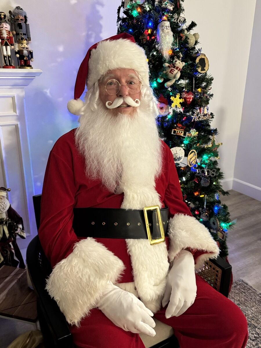 Santa Claus smiling warmly beside a lit Christmas tree